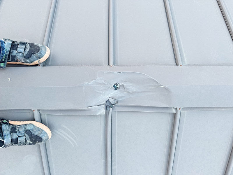 台風の飛来物で立平屋根の棟と本体が損傷している施工前の写真