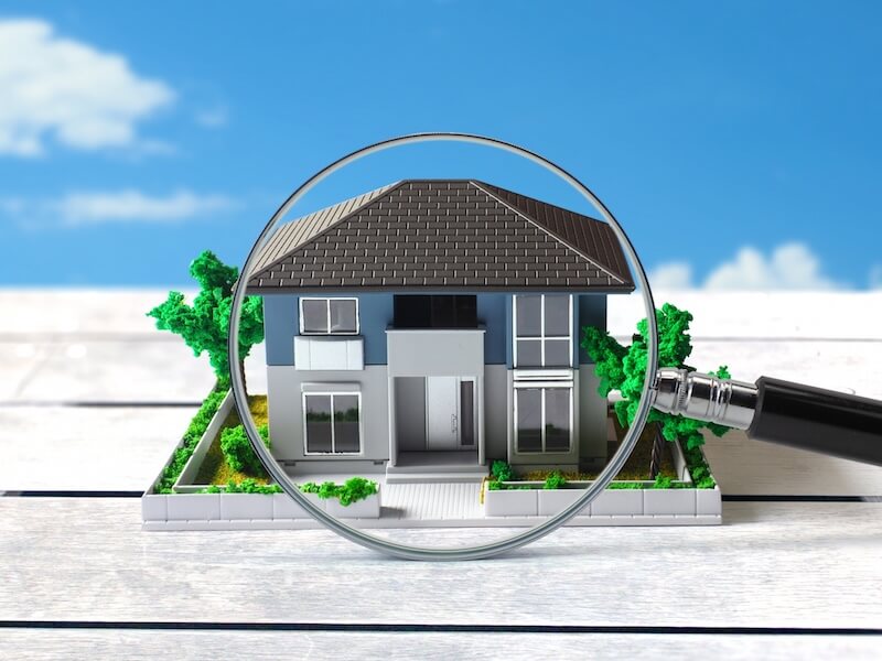 雨漏り調査のイメージ。住宅模型を拡大して確認する様子を表す拡大鏡の写真。